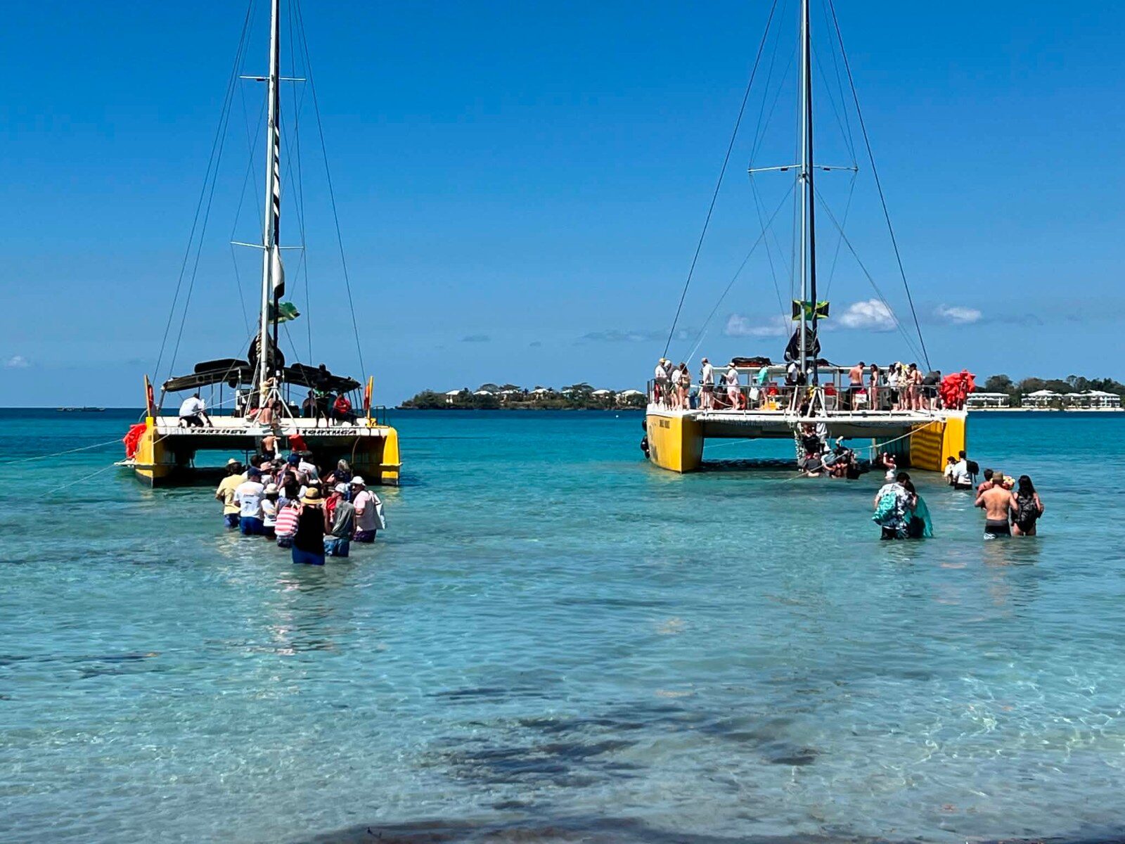 Deux catamarans ancrés en eau peu profonde, participants embarquant depuis la plage à Negril