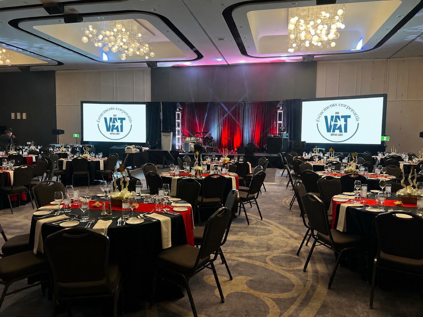 Salle de bal dressée pour une soirée gala d’entreprise, tables rondes et deux écrans géants