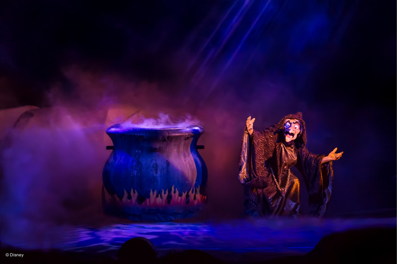 La sorcière de Blanche-Neige, bras tendus près d’un chaudron géant dans la fumée violette, pendant le spectacle Fantasmic, à Disney’s Hollywood Studios La sorcière de Blanche-Neige, bras tendus près d’un chaudron géant dans la fumée violette, pendant le spectacle Fantasmic, à Disney’s Hollywood Studios
