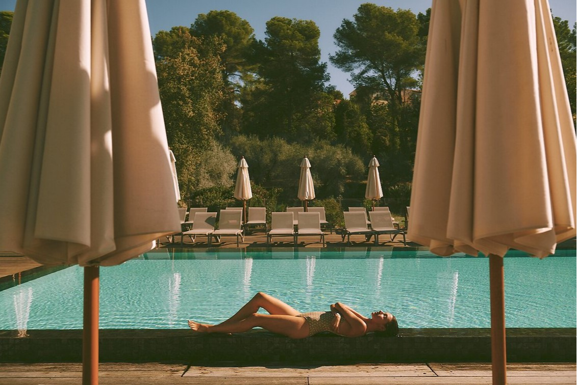 Woman relaxing by the pool at Club Med Opio in Provence, surrounded by loungers, umbrellas, and trees for a serene escape. Woman relaxing by the pool at Club Med Opio in Provence, surrounded by loungers, umbrellas, and trees for a serene escape.